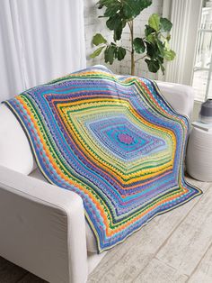 a crocheted blanket sitting on top of a couch next to a potted plant