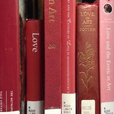 a row of red books sitting on top of a book shelf next to each other