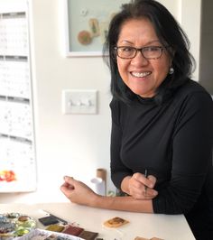 a woman sitting at a table in front of a calendar holding a pen and smiling