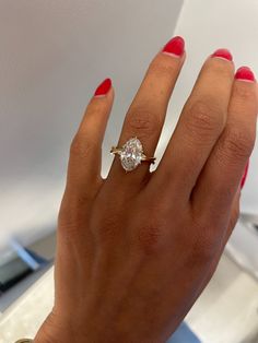 a woman's hand with red nails and a ring on her finger, holding an engagement ring