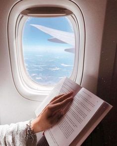 a woman reading a book while looking out an airplane window