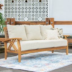 a wooden couch sitting on top of a rug next to a potted plant in front of a white wall