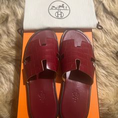 Hermes Is A Brand That Epitomizes Art And All Their Designs Have A Luxurious Blend Of Comfort And Style. These Brick Red Izmir Sandals Have Been Crafted From Exotic Leather In Italy And Feature The Iconic H On The Vamp, Making Them Easy To Slip On Over All Your Casual Outfits. A Necessity In Every Summer Wardrobe. Condition: Authentic, Brand New; Pristine; Never Been Worn Additional Info: Comes With 2 Dust Bags By The Brand Designer Slip-on Sandals With Red Sole, Classic Sandals With Red Sole, Luxury Red Sandals With Leather Sole, Luxury Red Slip-on Sandals, Luxury Red Flat Sandals, Hermes Izmir, Hermes Shoes, Brick Red, The Vamps