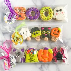 three decorated cookies in plastic wrappers on a marble counter with the word boo spelled out