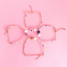 four bracelets with beads and eyeballs on pink background, close up view from above