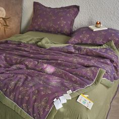 an unmade bed with purple and green bedspread on top of it next to a painting