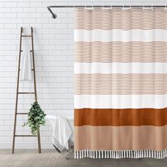 a shower curtain with an orange and brown striped design on it, next to a white brick wall