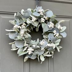 a wreath with white flowers and green leaves hangs on the front door's gray paneled door