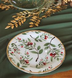 a white plate with red berries and green leaves on it sitting on a table cloth