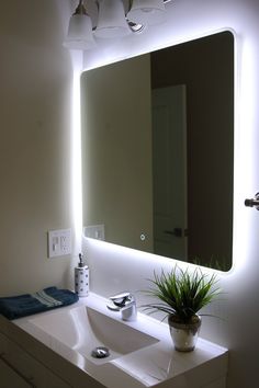 a bathroom sink under a large mirror with lights on it and a plant in the corner