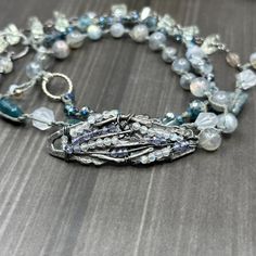 This incredible wrap bracelet has been a work in progress for a while. The combination of the pewter focal with the gorgeous 6mm flashy labradorite rounds absolutely enchanted me. From there, I added so many of my favorite things. In this bracelet, you’ll find apatite rectangles, the most insane faceted 8mm kyanite, 8mm starcut pale jade, flashy tourmilinated rainbow moonstone, smoky quartz, and the most incredible faceted prasiolite nuggets. Also featured are the prettiest faceted glass rondelles. Let’s circle back to the focal. The shape was so interesting and mysterious to me. I wrapped on faceted labradorite and iolite to bring out some of the lines. This wrap bracelet is sterling silver, with the exception of the USA made pewter focal. The knotted portion of the bracelet was done in h Artisan Silver Beaded Bracelets With Unique Variations, Silver Multi-strand Hand Wrapped Bracelets, Silver Hand Wrapped Beaded Bracelets For Healing, Silver Gemstone Beads Wrap Bracelet, Silver Multi-strand Spiritual Bracelets, Silver Gemstone Beads Wrap Bracelet As Gift, Silver Double Strand Bracelet With Natural Stones, Silver Double Strand Beaded Bracelets With Gemstones, Silver Wrap Bracelet With Gemstone Beads