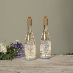 two glass bottles with floral designs on them sitting next to some purple and white flowers