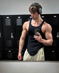 a man standing in front of lockers with headphones on and looking at his cell phone