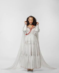 a woman wearing a white dress and holding her hands up to the side while standing in front of a white background