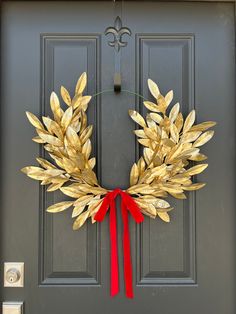 a gold wreath with red ribbon hanging on a gray front door, decorated with golden leaves