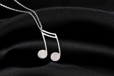 a music note necklace on a black cloth with a silver chain hanging from the neck