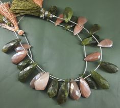 a necklace made with green and pink stones, tassels and other items on a table