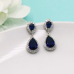 "Add a touch of sparkle and look of diamonds with these classically designed framed pave cubic zirconia teardrop wedding earrings featuring a royal sapphire blue shade set in brilliant yellow gold. Measuring 1 1/4\" long, these are perfect for any special occasion. All jewelry features high quality electroplating that does not fade or chip and is nickel free (hypoallergenic). Orders are shipped via USPS with tracking and confirmation. Item arrives in a complimentary gift box. ------------------- Blue Diamond Drop Earrings With Prong Setting, Blue Cubic Zirconia Crystal Earrings, Blue Cubic Zirconia Diamond Earrings For Formal Events, Blue Diamond Drop Earrings With Accents, Blue Cubic Zirconia Earrings With Sparkling Stones, Blue Cubic Zirconia Diamond Earrings With Prong Setting, Blue Cubic Zirconia Earrings With Prong Setting, Sapphire Crystal Drop Earrings For Formal Occasions, Blue Cubic Zirconia Drop Earrings