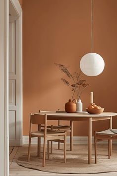 a dining room with an orange painted wall and wooden table surrounded by chairs, vases and plants