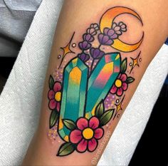 a colorful tattoo on the arm of a woman with flowers and an emerald stone in it