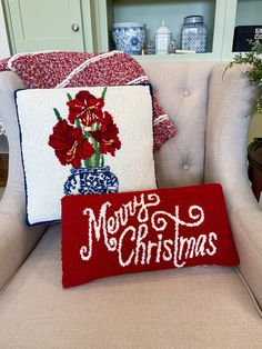 two christmas pillows on a chair in front of a shelf with vases and flowers