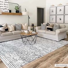 a living room with white couches and black and white pillows on top of the rug