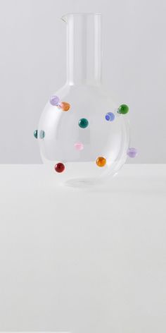 a glass vase with multicolored dots on the top and bottom, sitting on a white surface