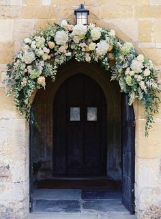 the entrance to an old building with flowers on it's arch and light fixture