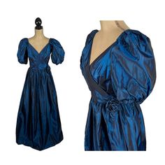 80's does Victorian in this midnight blue taffeta short sleeve evening gown that was ILGWU union made in the USA. This iridescent formal dress has a full, floor length skirt, fitted waist with rosette accent, surplice v- neck and BIG puff balloon sleeves. Perfect for a 1980's themed prom, gala or princess ball. The dress in unlined and has a back zipper.     MEASUREMENTS: Armpit to armpit - 14 inches Bust fits up to - 34 inches Waist - 27 inches Hips - 50 inches Length - 56 inches Modern size: S Big Puff Sleeves, 1980s Prom Dress, 1980s Prom, Blue Formal Dress, Evening Gowns With Sleeves, Blue Dress Formal, Iridescent Blue, Floor Length Skirt, Balloon Sleeves