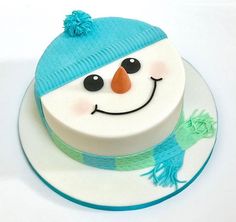 a frosted cake with a blue hat and scarf on it's face, sitting on a plate