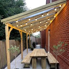 a wooden bench sitting under a pergolated covered patio with lights strung over it