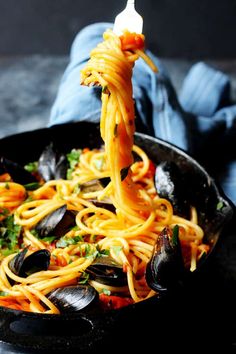 spaghetti being lifted from a skillet with mussels