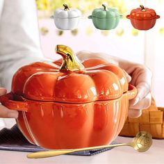 a person holding an orange pumpkin shaped casserole with spoons in front of it