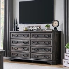 a large tv mounted on the wall above a dresser in a room with gray curtains