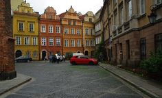 the red car is parked on the cobblestone street in front of old buildings