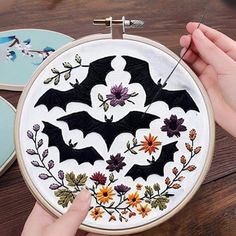 someone is working on some embroidery work with flowers and bats in the hoop, while another hand holds a needle