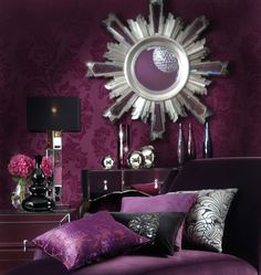 a living room with purple walls and pillows on the chaise longue in front of a large sunburst mirror