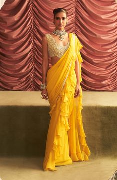 Brighten up any occasion with this yellow embellished blouse, beautifully paired with a pre-draped ruffle sari. The intricate embellishments add a touch of sophistication, while the playful ruffles bring a modern twist, making this ensemble perfect for festive celebrations and stylish gatherings. Ruffled Pre-draped Saree For Diwali, Designer Bollywood Style Ruffled Sharara, Designer Bollywood Style Sharara With Ruffles, Bollywood Designer Wear Sharara With Ruffles, Bollywood Style Designer Ruffles Sharara, Navratri Ruffled Sharara Saree, Designer Georgette Blouse With Ruffles, Ruffled Saree Blouse For Wedding, Designer Ruffled Blouse Piece For Diwali