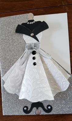 a dress made out of paper on top of a piece of silver glittered paper