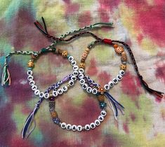 three bracelets with beads and charms on a tie dye cloth covered tablecloth background