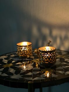 two lit candles sitting on top of a black and white table next to each other