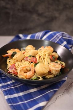 pasta with shrimp and spinach in a black bowl on a blue towel next to a fork