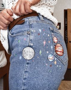 a woman is showing off her jeans with space patches on the bottom, and planets on the back