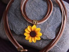 a yellow flower is sitting on top of a brown leather cord with a gold clasp