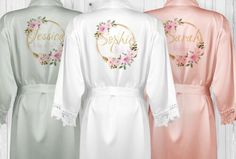 three robes with embroidered names and flowers on them, one is pink, the other is white