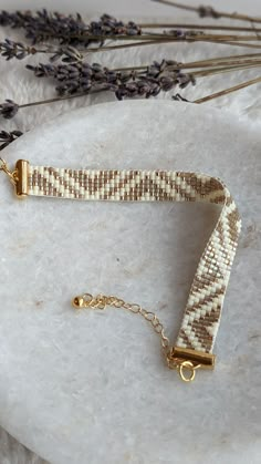 a white and gold bracelet sitting on top of a marble slab next to lavender flowers