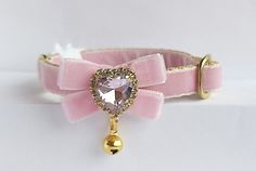 a pink bow tie with a heart shaped brooch on it's side and a gold bell