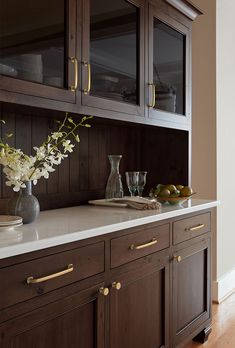 a kitchen with wooden cabinets and marble counter tops, along with white flowers in a vase