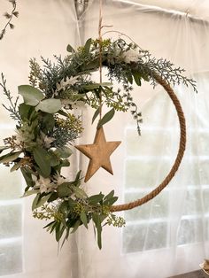 a christmas wreath hanging from a rope with greenery and a star on it in front of a window