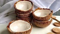 four coconut shell bowls with wooden spoons next to them on a white tablecloth